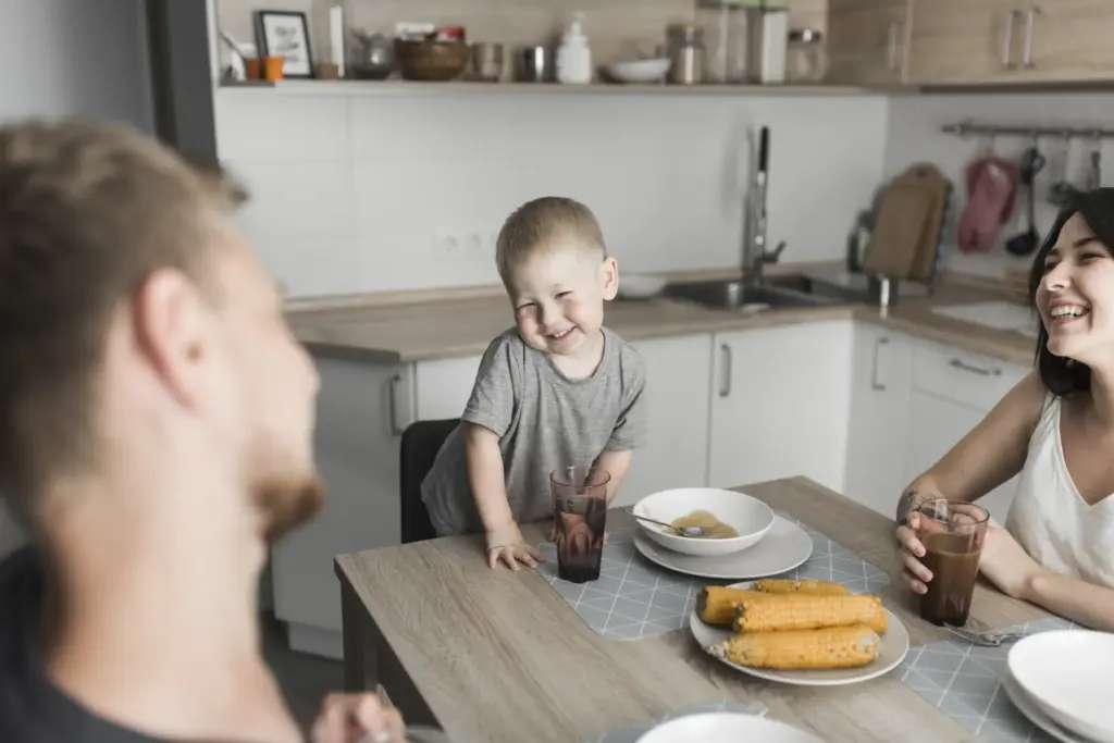 Niño pequeño desayunando con una persona adulta en una cocina luminosa.